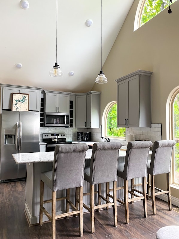 A modern kitchen with grey cabinets, stainless steel appliances, and a central island with bar stools.