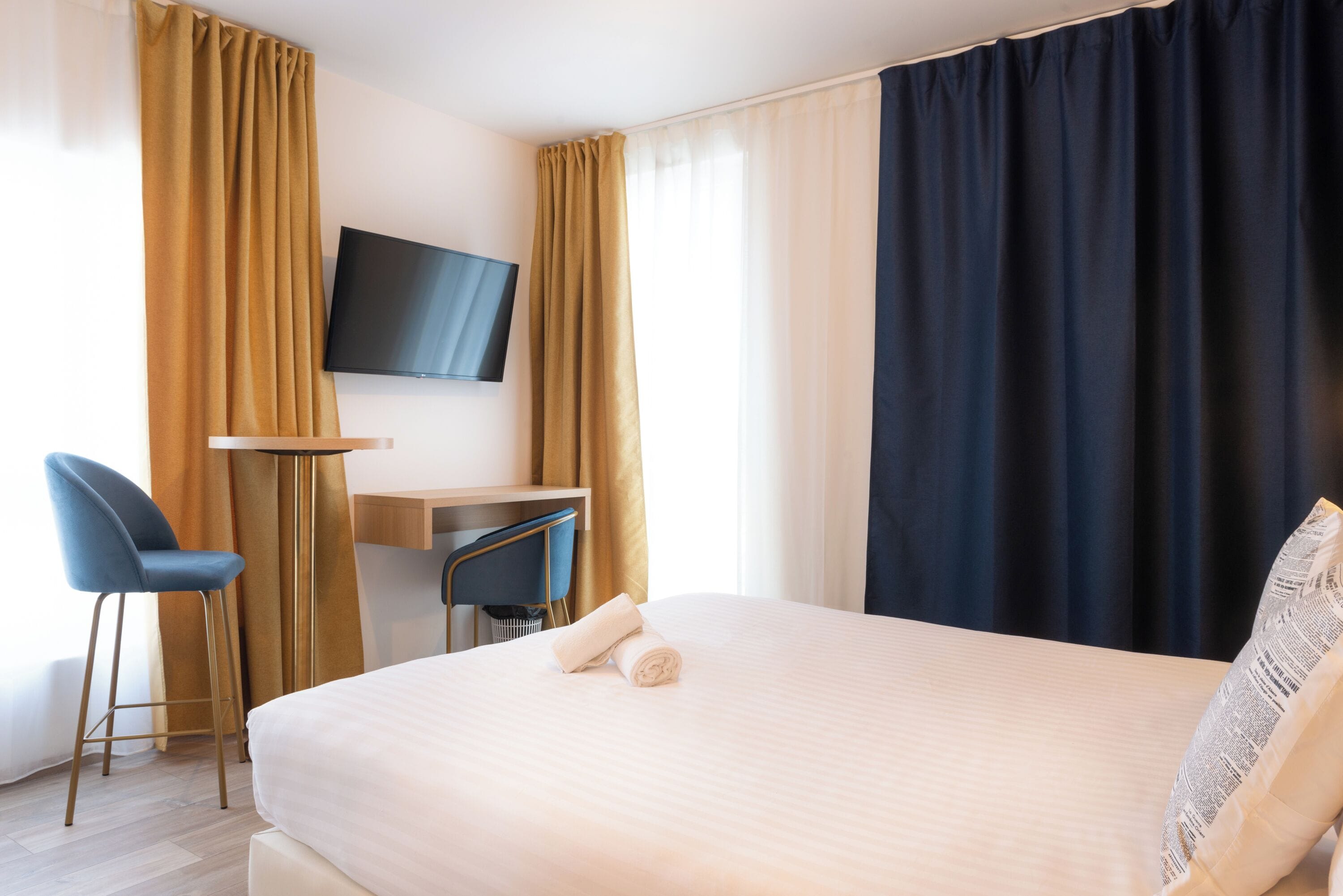 A hotel room with a bed, a desk, a chair, a TV, and curtains.
