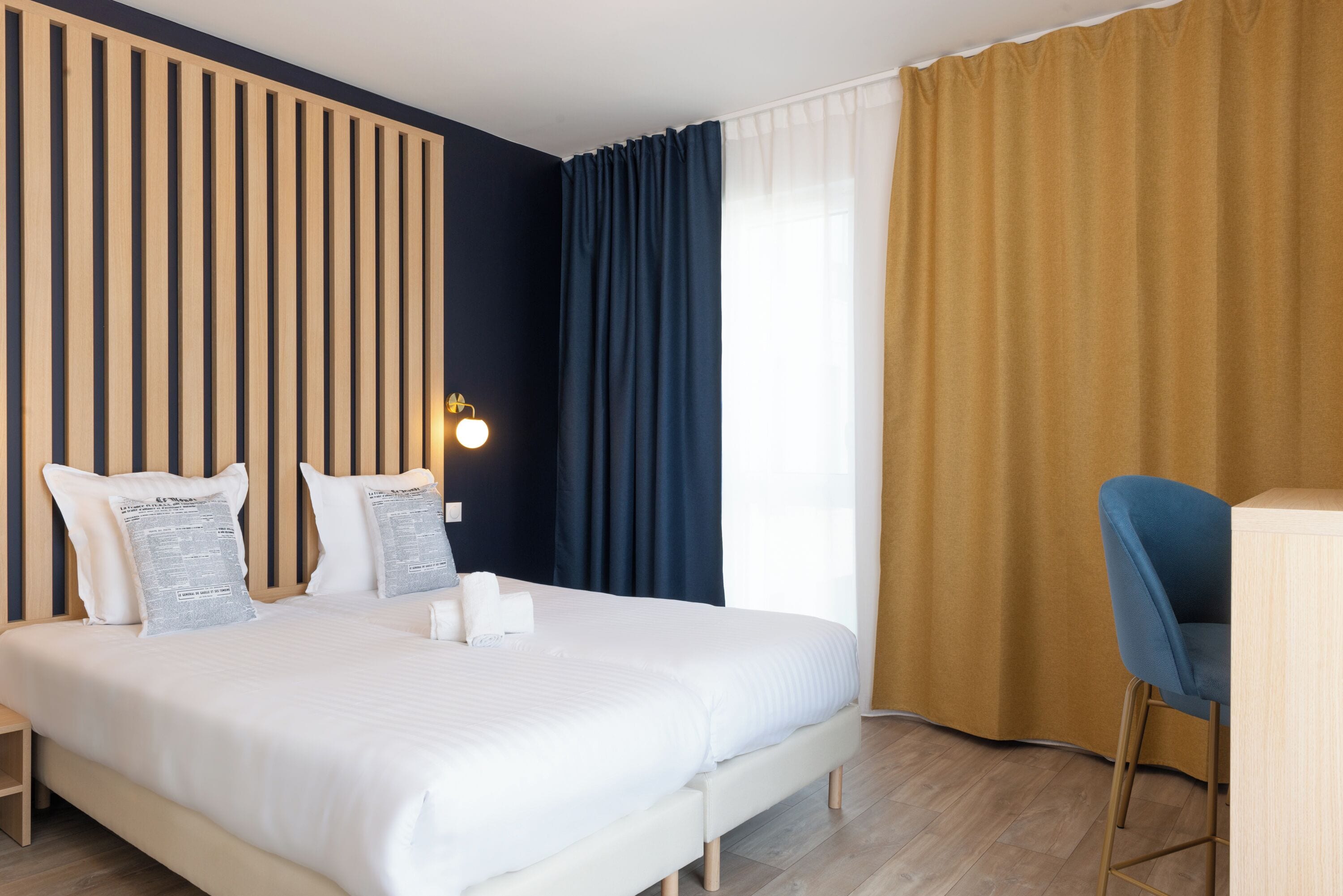 Habitació d'hotel amb un llit gran, una taula de treball amb una cadira i una finestra amb cortines.