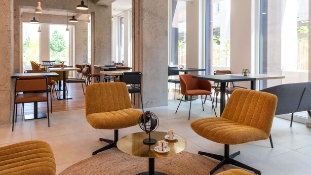 A modern interior with large windows, a central seating area with two chairs, and a dining area with tables and chairs. -  Aparthotel Adagio Access Paris Ivry Confluence (Ivry-sur-Seine)