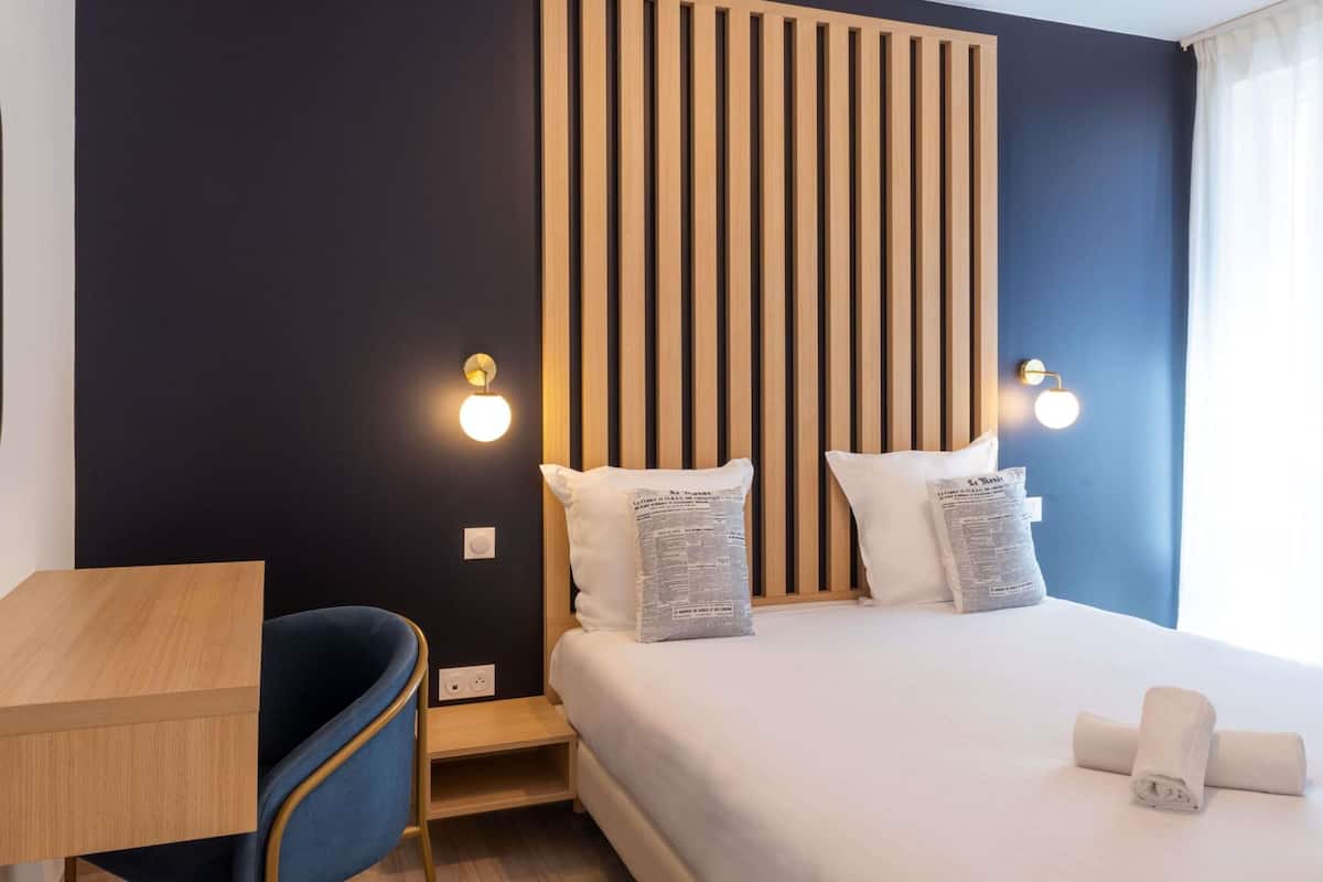 A hotel room with a bed, bedside tables, a desk, and a chair.