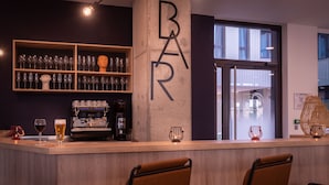 A bar area with a concrete pillar displaying 'BAR', shelves with glasses, a coffee machine, and two chairs in front. -  Aparthotel Adagio Access Paris Ivry Confluence (Ivry-sur-Seine)