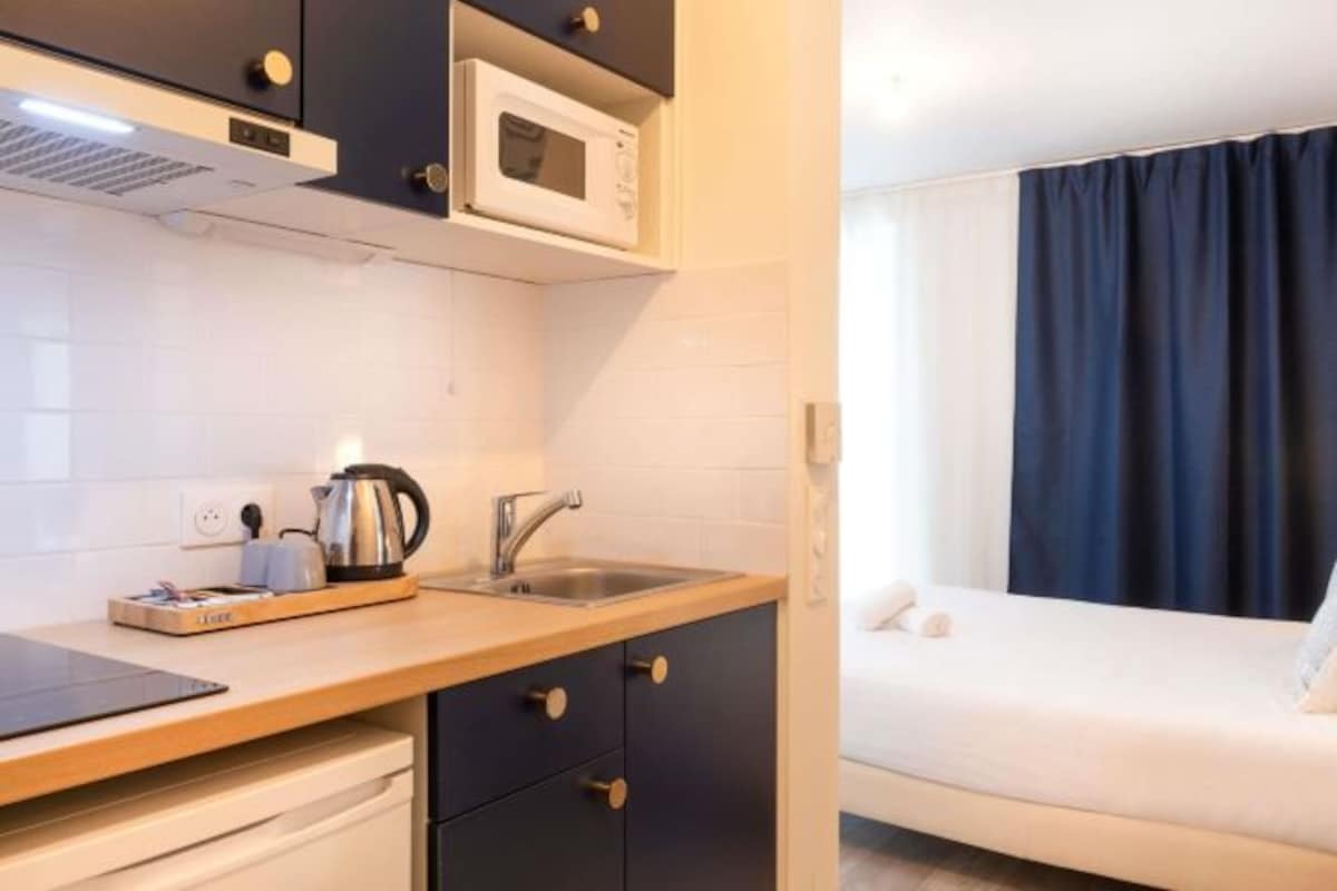 Habitación de hotel compacta con kitchenette, cama y ventana con cortinas.