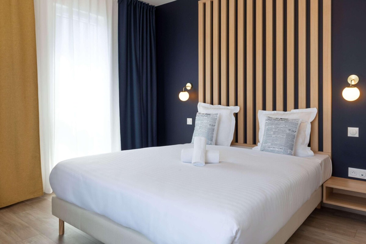 Una habitación de hotel moderna con una cama grande, un cabecero de madera y dos luces fijadas a la pared.