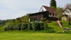 A modern two-story house with a red roof, surrounded by lush greenery and a small red slide. - Vacations with a view of the Argen, an oasis of peace in the Argen Valley (Neukirch)