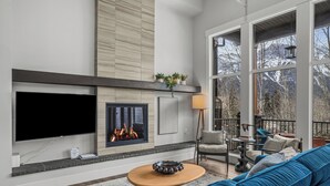 A modern living room with a fireplace, large windows, and a blue sofa. - M3- Serene Canmore Retreat- A/C, Free EV Charge, 5BD, 4.5BT, Hot Tub, Mtn View (Canmore)
