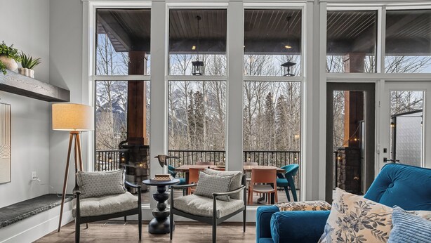 A cozy interior with a sofa, chairs, a lamp, and a view through large windows. - M3- Serene Canmore Retreat- A/C, Free EV Charge, 5BD, 4.5BT, Hot Tub, Mtn View (Canmore)
