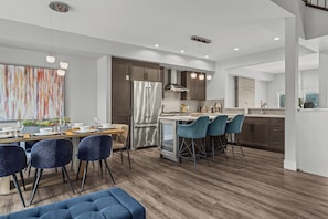 Une cuisine moderne dotée d’un îlot central, de meubles en bois foncé, d’appareils électroménagers en acier inoxydable et de chaises bleues.