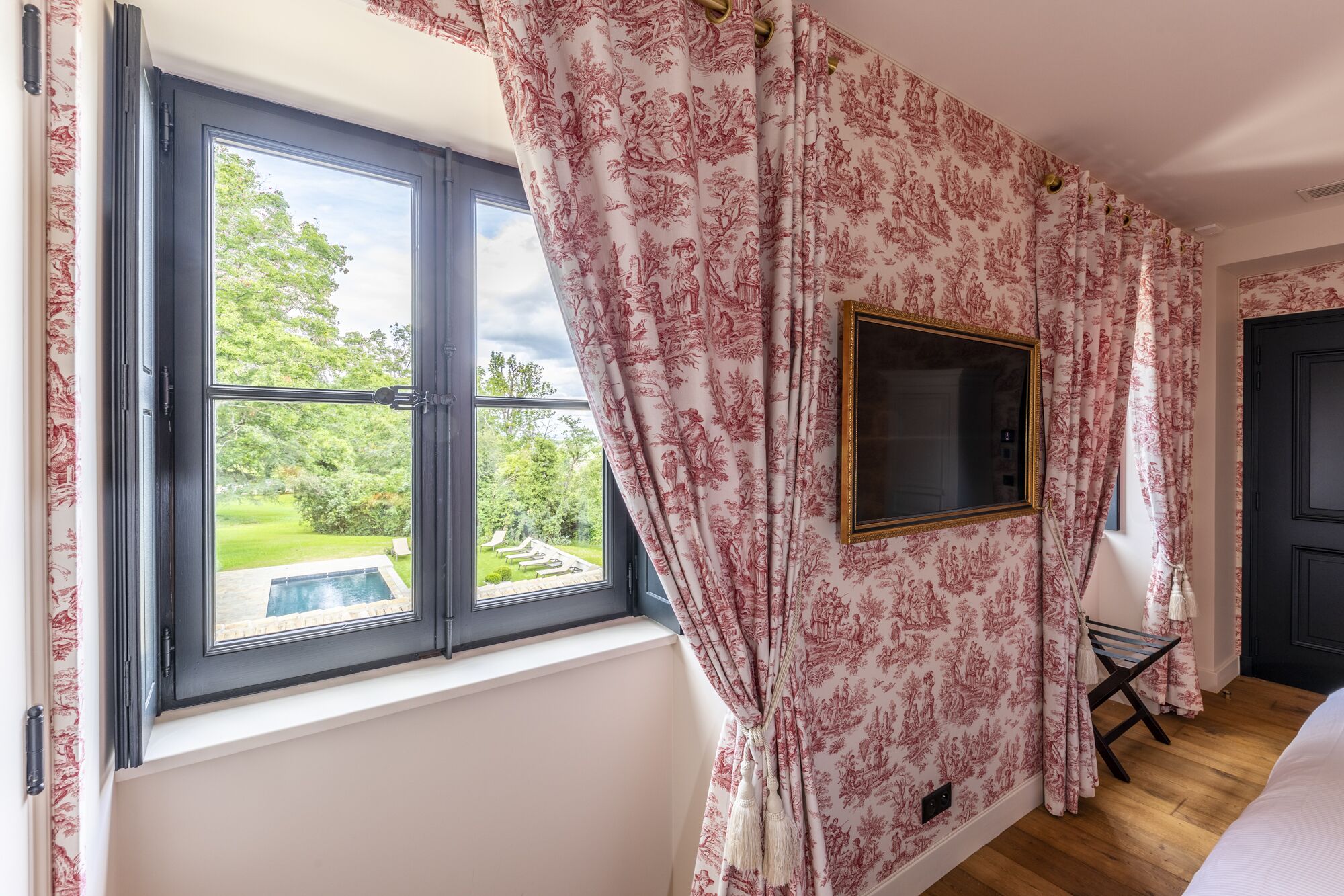 Ein Zimmer mit einem großen Fenster, einem gerahmten Spiegel und Blick auf einen Pool sowie Grünflächen.