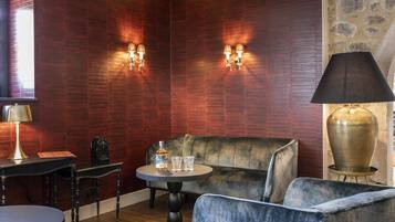 A room with a dark wood panel wall, a round table with a bottle and glasses, a sofa, a lamp, and a vintage-style radio.