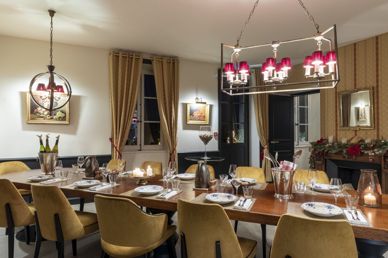 A dining room with a long table set for a meal, featuring a chandelier, candles, and a fireplace with festive decorations.