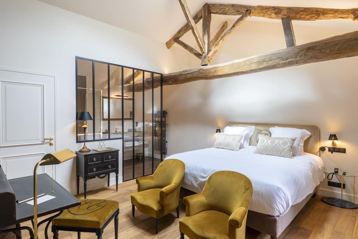 Un dormitorio con una cama grande, dos sillones, un escritorio y un espejo.