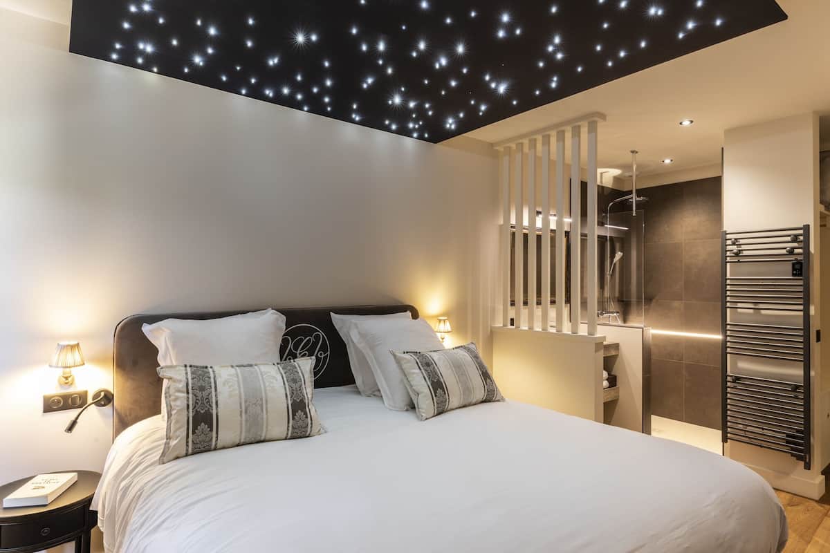 Un dormitorio moderno con cama, lámparas de noche y un techo con luces que simulan estrellas.