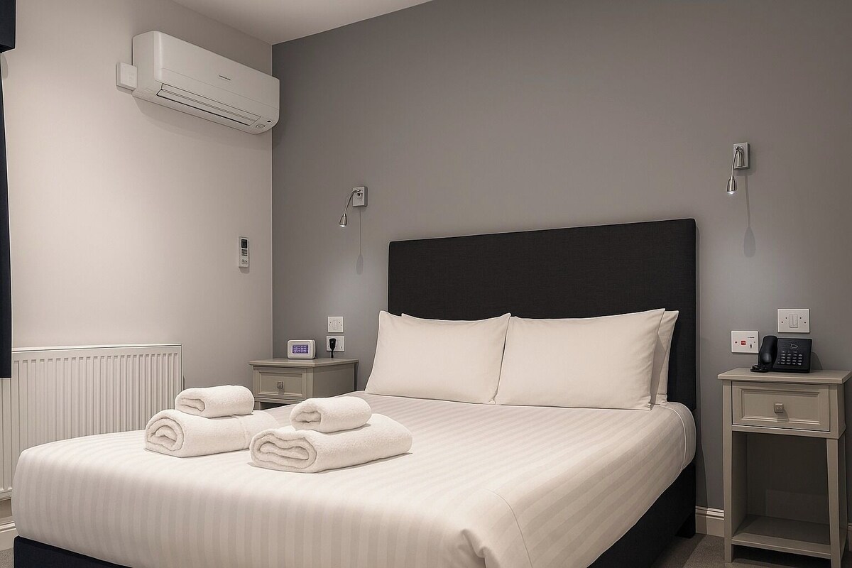 A modern hotel room with a large bed, two bedside tables, an air conditioning unit, and a thermostat.