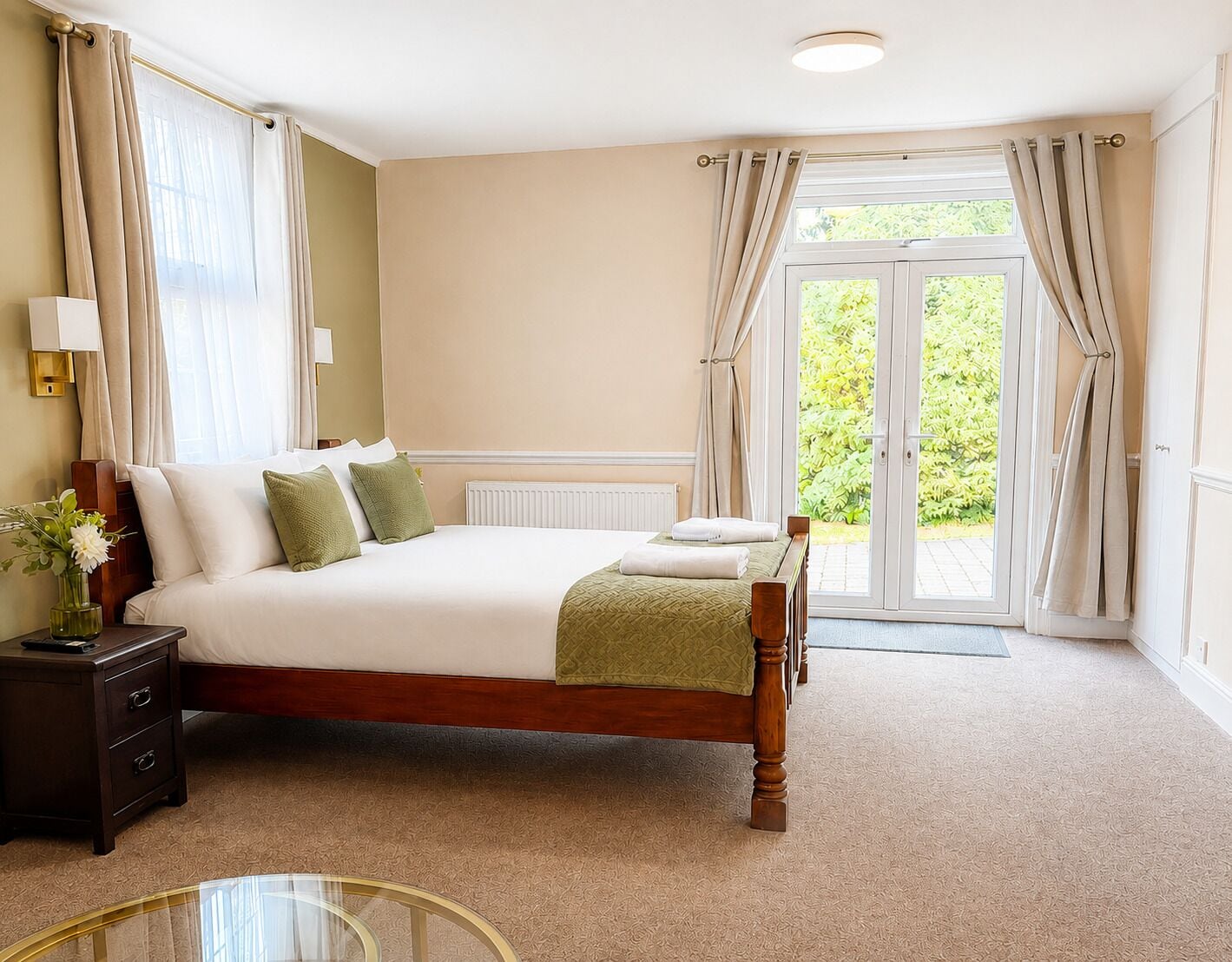 Habitación de hotel con una cama grande, una mesita de noche, una lámpara y vistas a zonas verdes a través de la puerta.