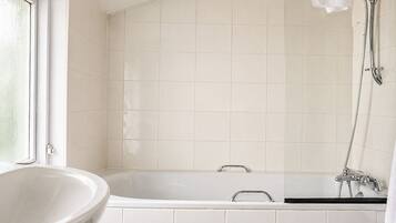 Een badkamer met een vrijstaand bad, een raam en een douchegedeelte.