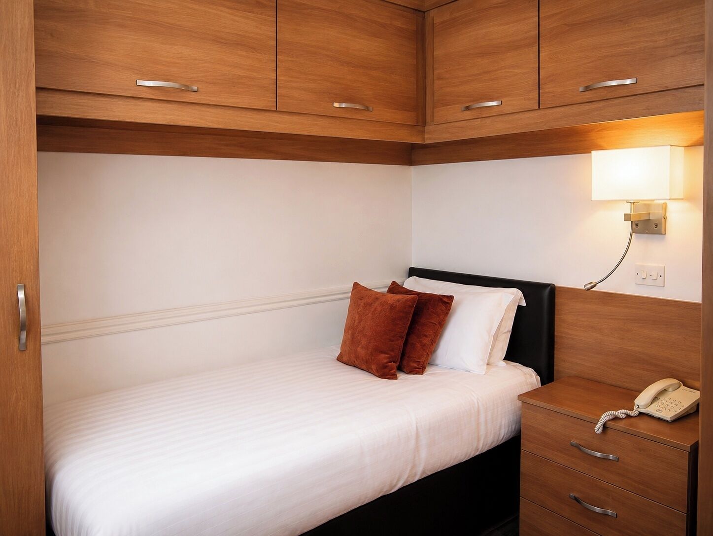 A hotel room with a bed, a bedside telephone, and a wall-mounted light.