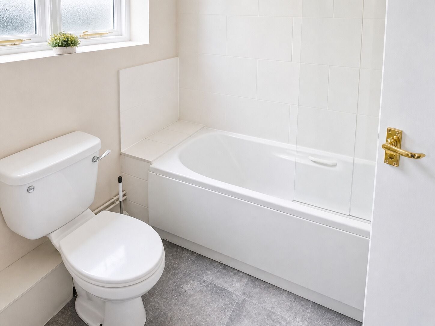 A bathroom with a toilet, bathtub, and a window with a plant.