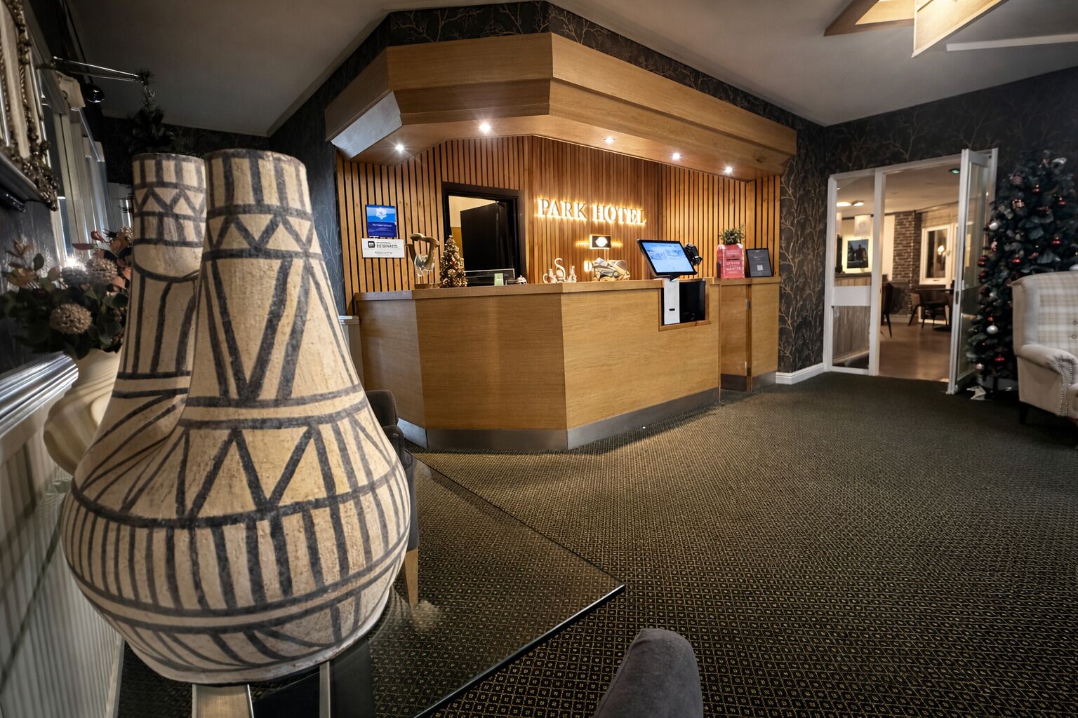 Zona de recepción de un hotel con mostrador de madera, pantalla digital y un árbol de Navidad.