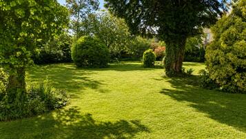 A well-maintained garden with a variety of trees and shrubs, a neatly trimmed lawn, and a clear sky.