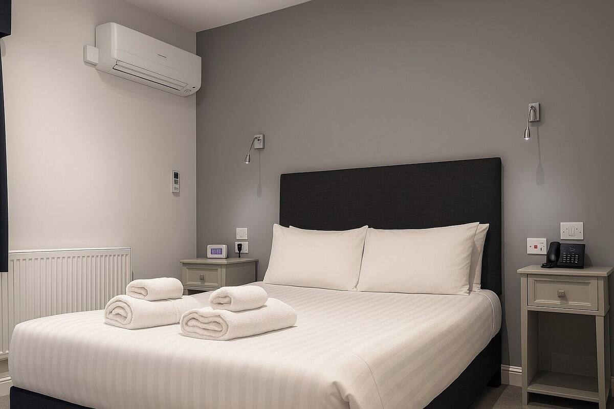 A modern hotel room with a large bed, two bedside tables, an air conditioning unit, and a thermostat.