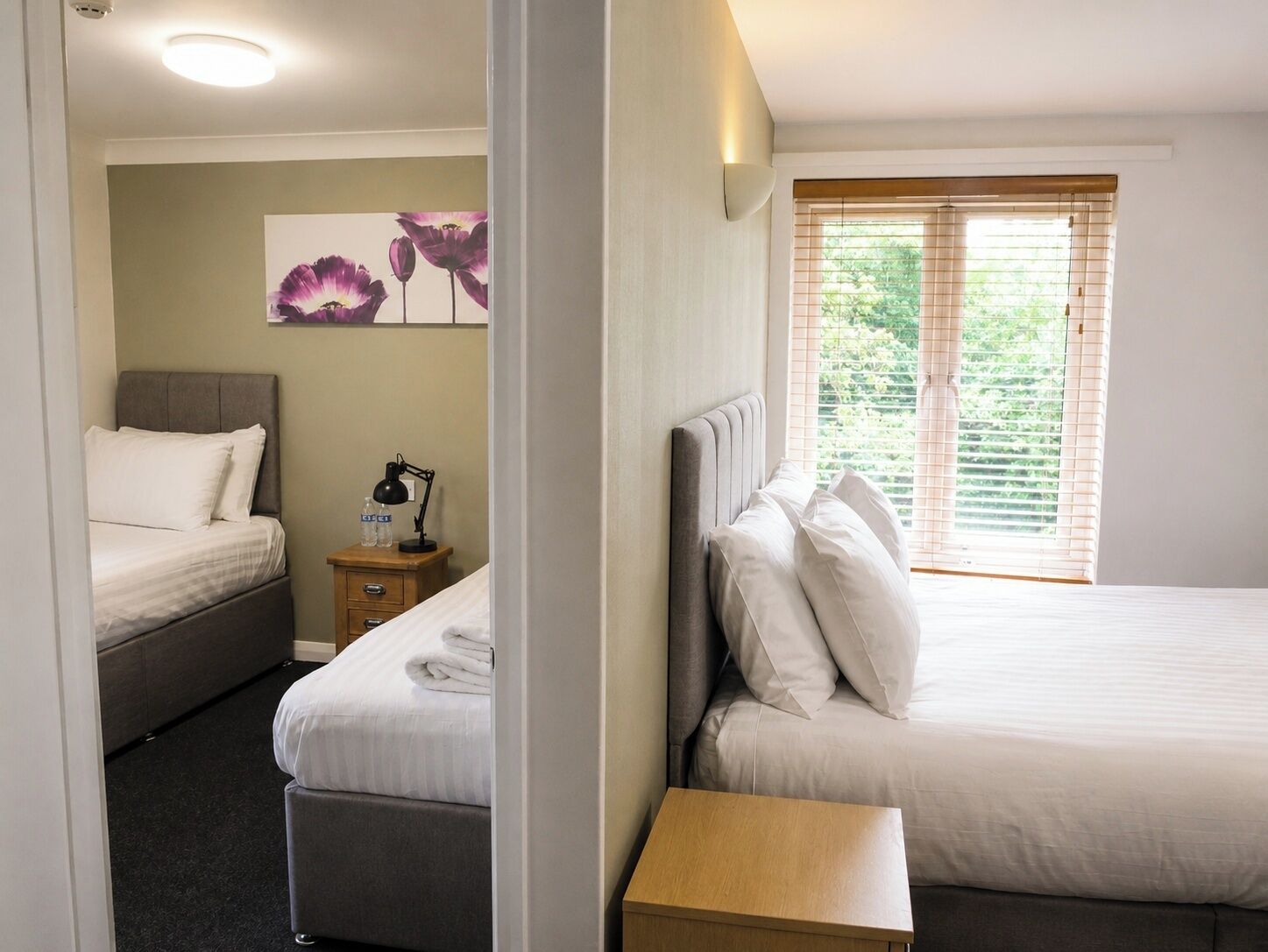 A hotel room with two beds, a nightstand with a lamp, and a painting on the wall.
