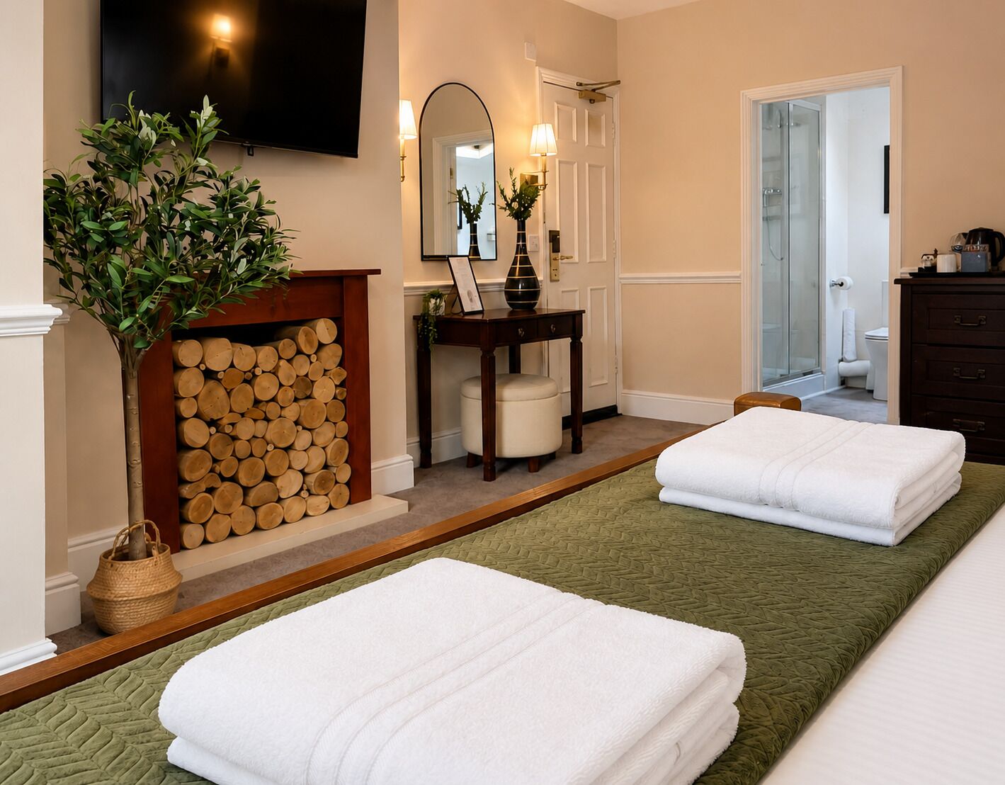 Habitación de hotel con cama, mesita de noche, espejo, chimenea con leña y televisor montado en la pared.