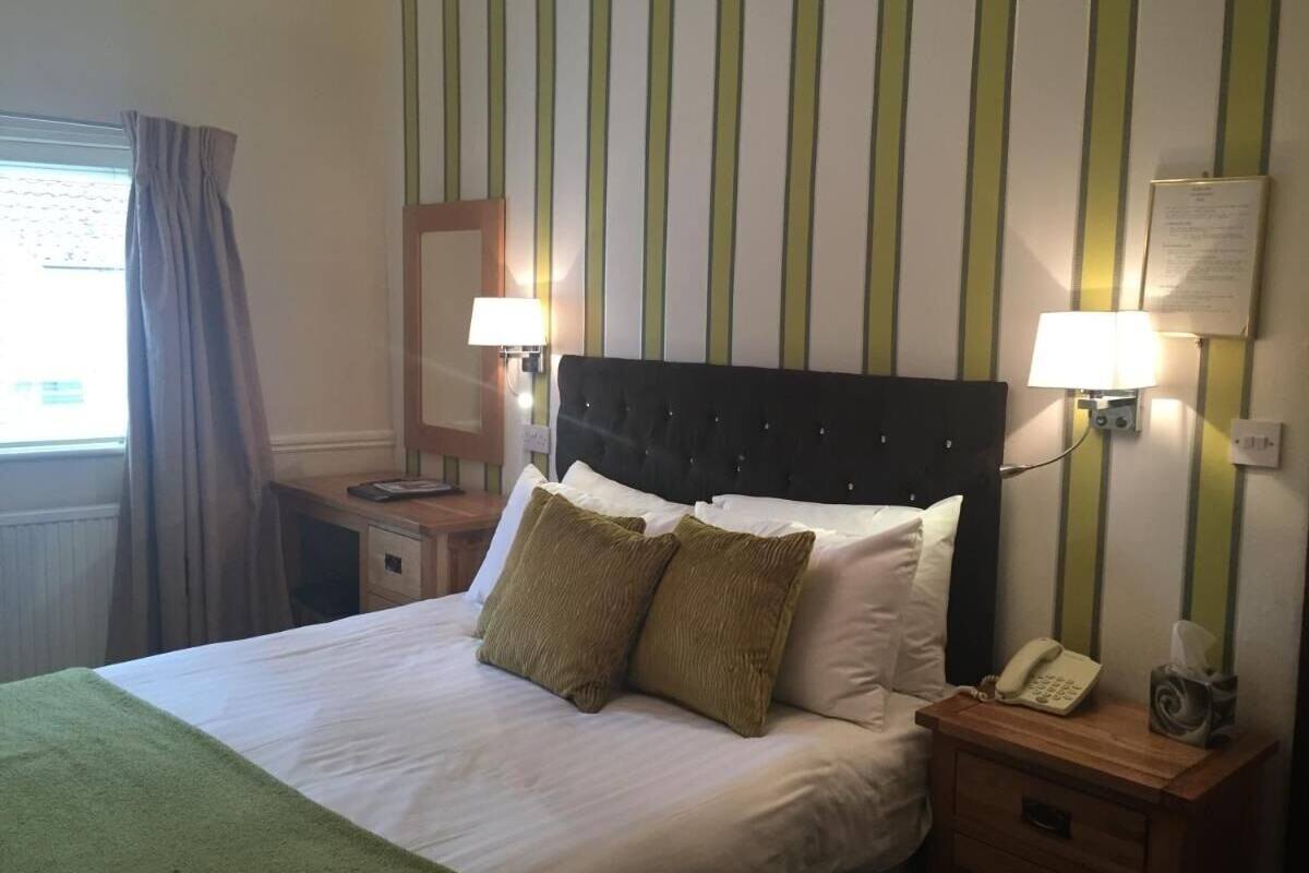 A hotel room with a bed, two bedside lamps, a telephone, and a window with curtains.
