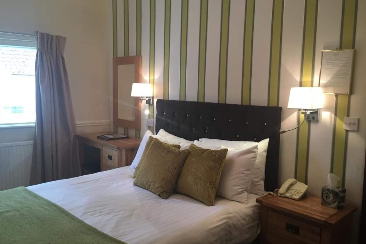 A hotel room with a bed, two bedside lamps, a telephone, and a window with curtains.
