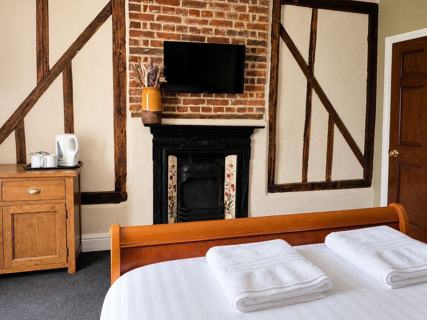 A hotel room with a bed, a TV mounted above a fireplace, a wooden dresser, and a door.