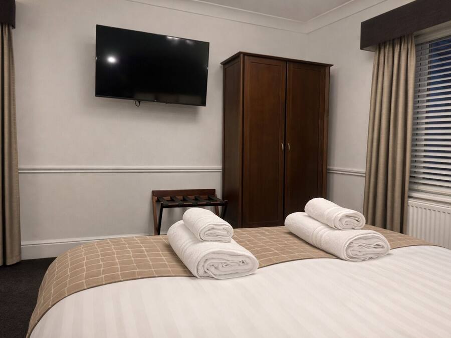 A hotel room with a bed, a TV mounted on the wall, a wardrobe, and a window with blinds.
