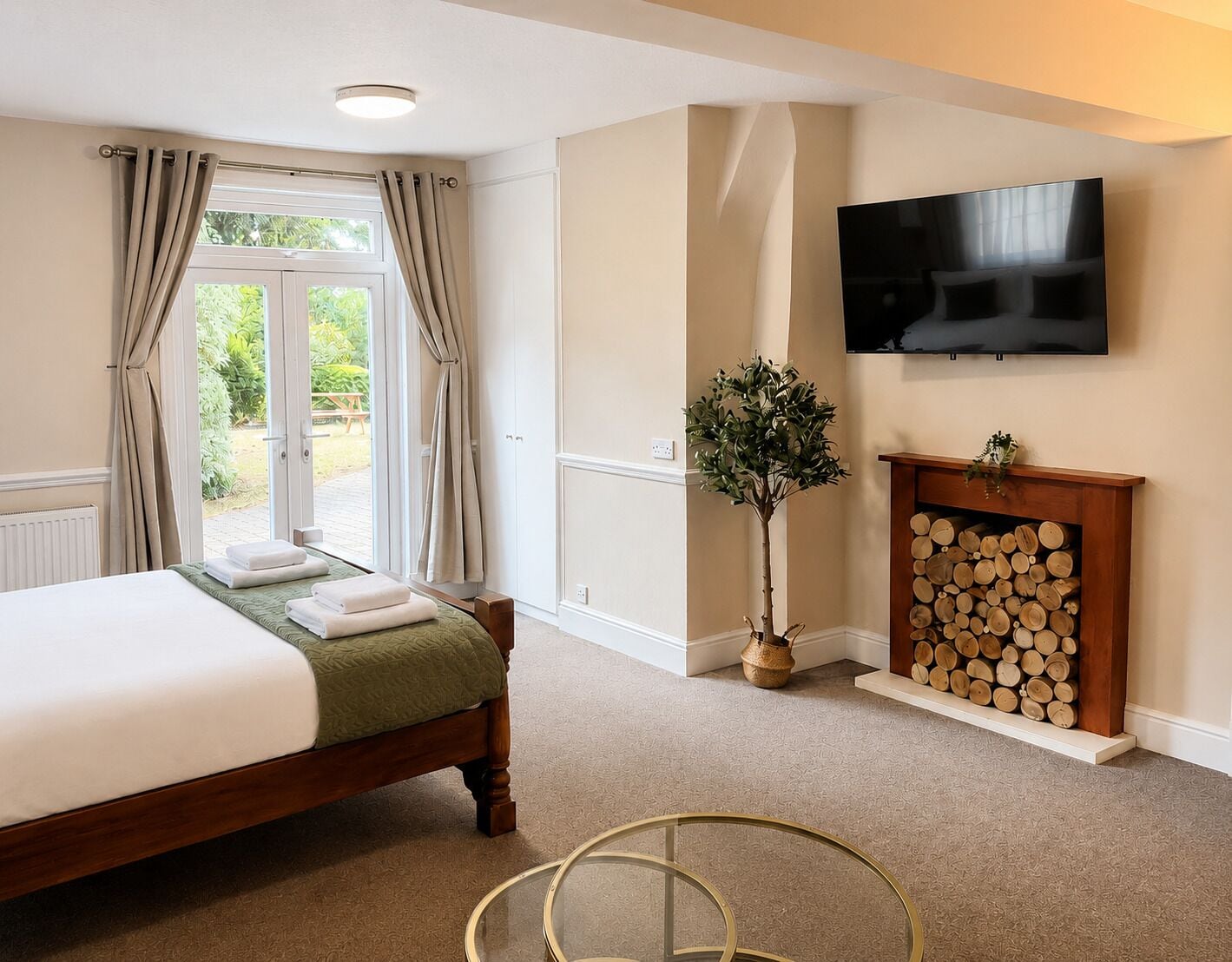 A bedroom with a bed, a television mounted on the wall, a fireplace with logs, and a window with curtains.
