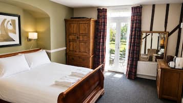 A hotel room with a large bed, a wardrobe, a radiator, a mirror, and a view of the garden through the door.