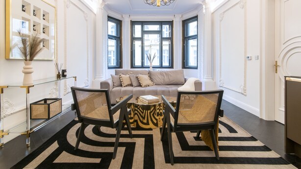 Un salon spacieux doté d’une grande fenêtre, d’un canapé, de deux fauteuils, d’une table basse et d’un lustre.