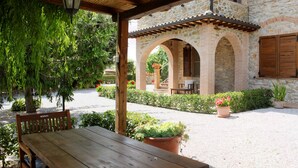 A covered patio with a wooden table and chairs, stone walls, and potted plants.