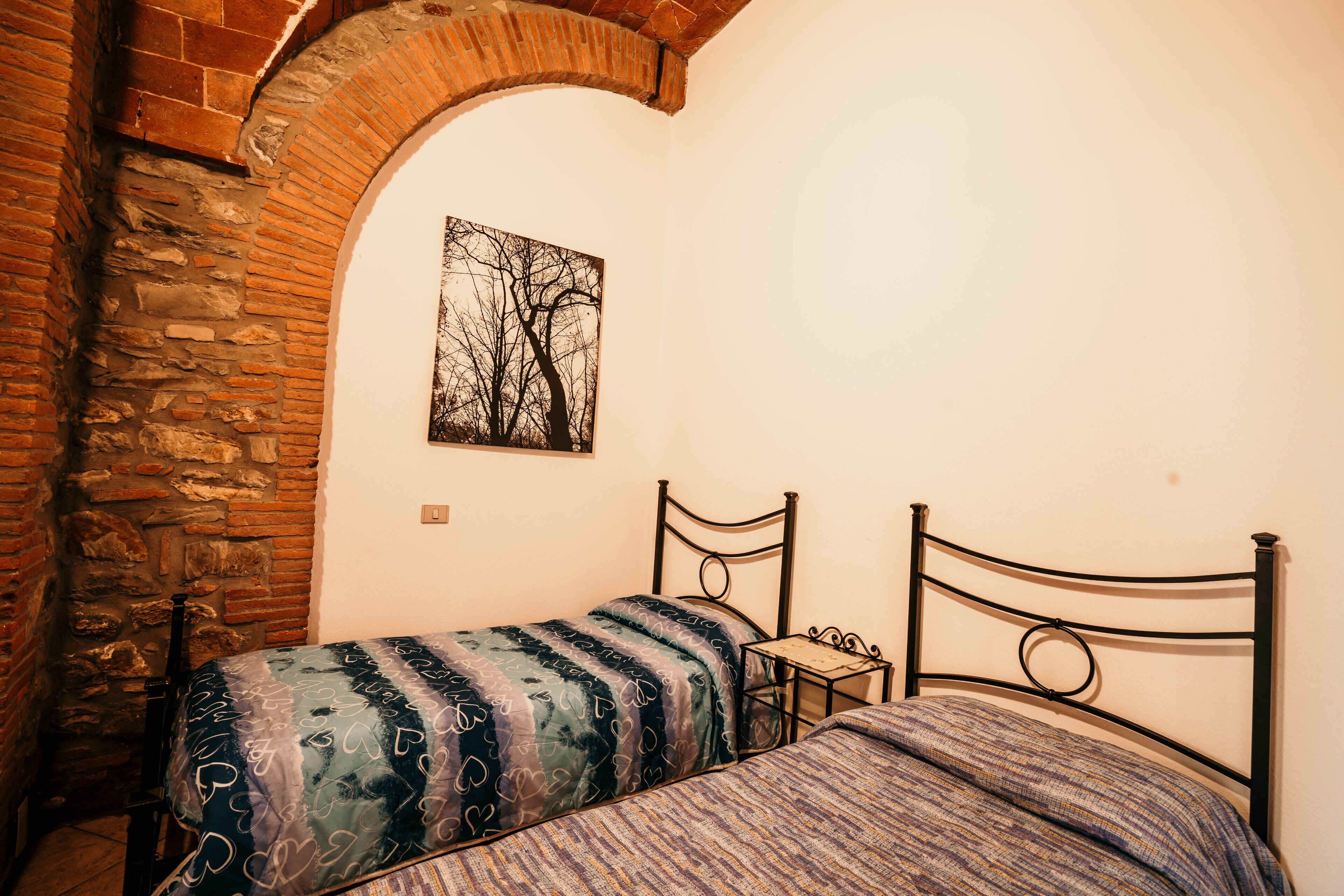 Una habitación pequeña con dos camas, una pared de piedra y un cuadro de árboles.