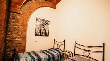 Una habitación pequeña con dos camas, una pared de piedra y un cuadro de árboles.