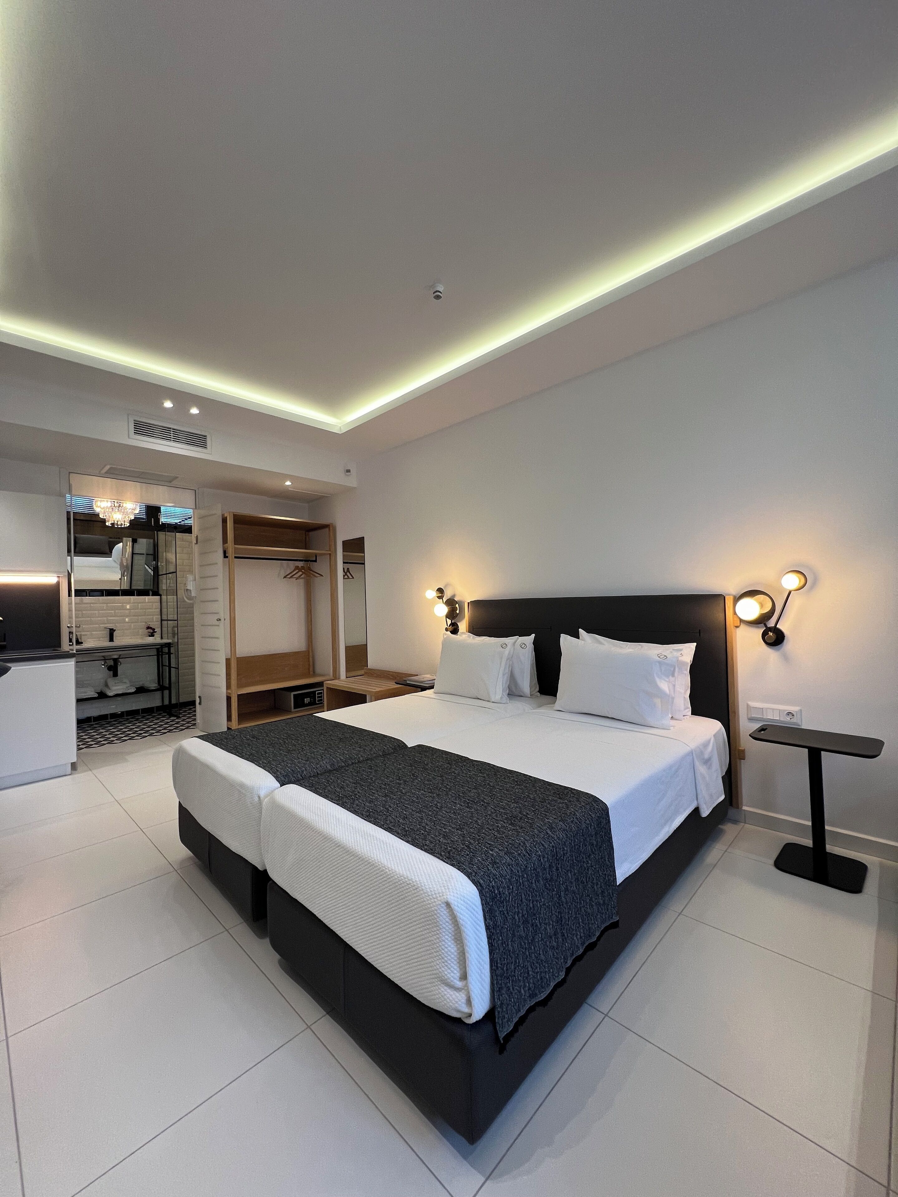 A modern hotel room with a large bed, bedside tables, a desk, and a wardrobe.