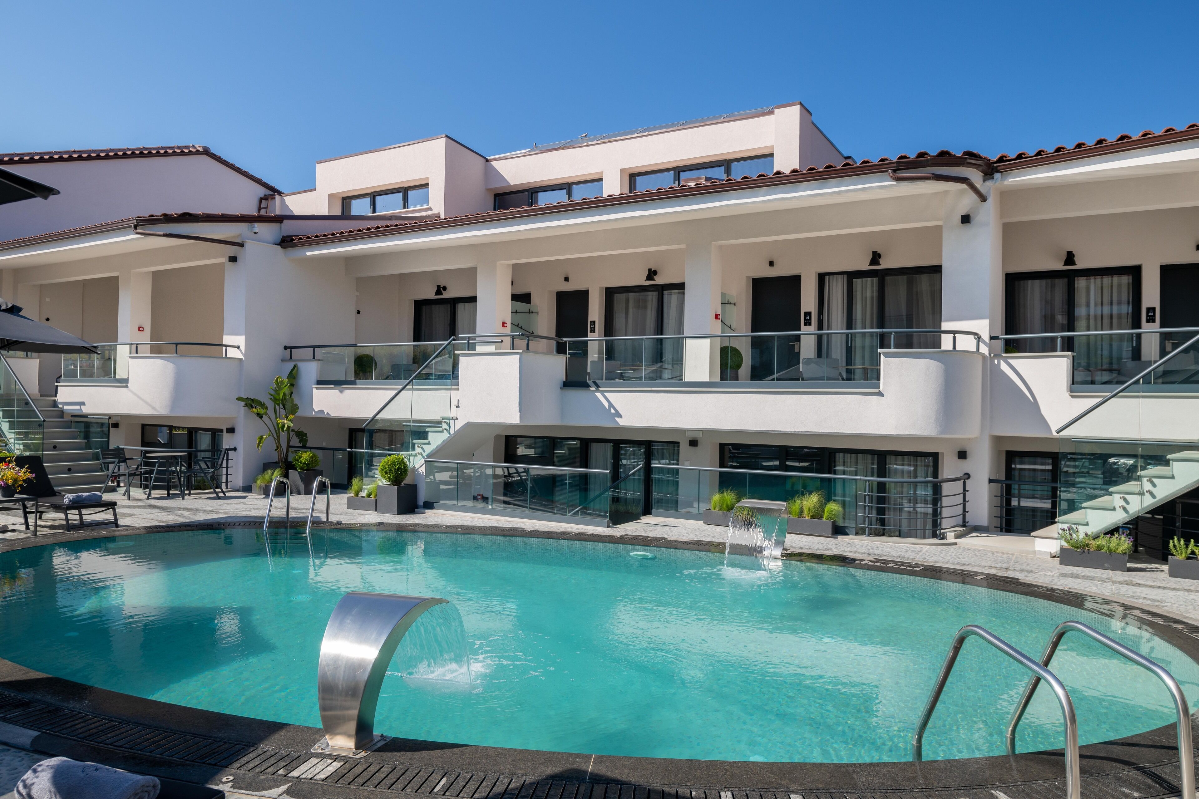 A modern hotel with a swimming pool, outdoor seating, and a covered terrace.