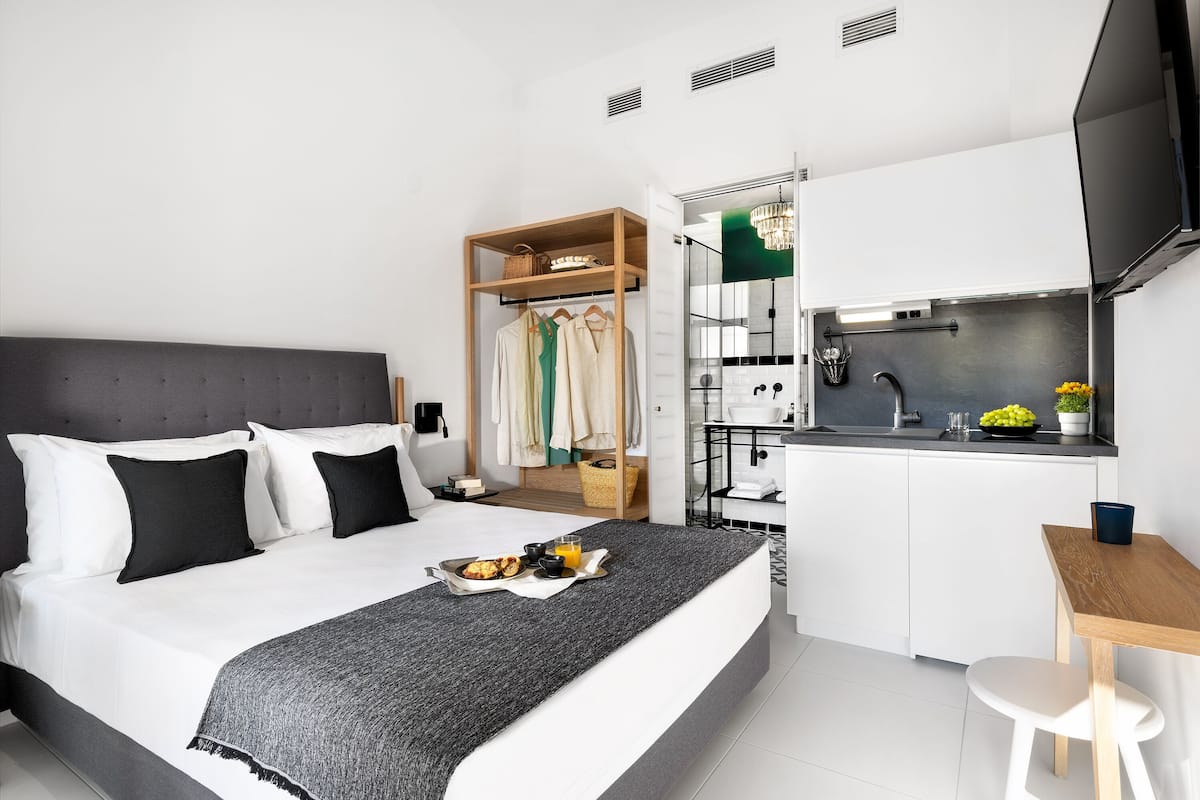Ett modernt hotellrum med en säng, ett litet pentry, en garderob i trä och en matplats.