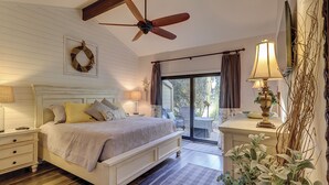 Ein Schlafzimmer mit einem Bett, Nachttischen, einem Deckenventilator, einem Fenster mit Vorhängen und Blick ins Freie.