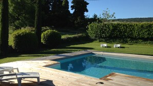 Uma piscina retangular com deck de madeira, rodeada por um gramado bem cuidado e sebes.