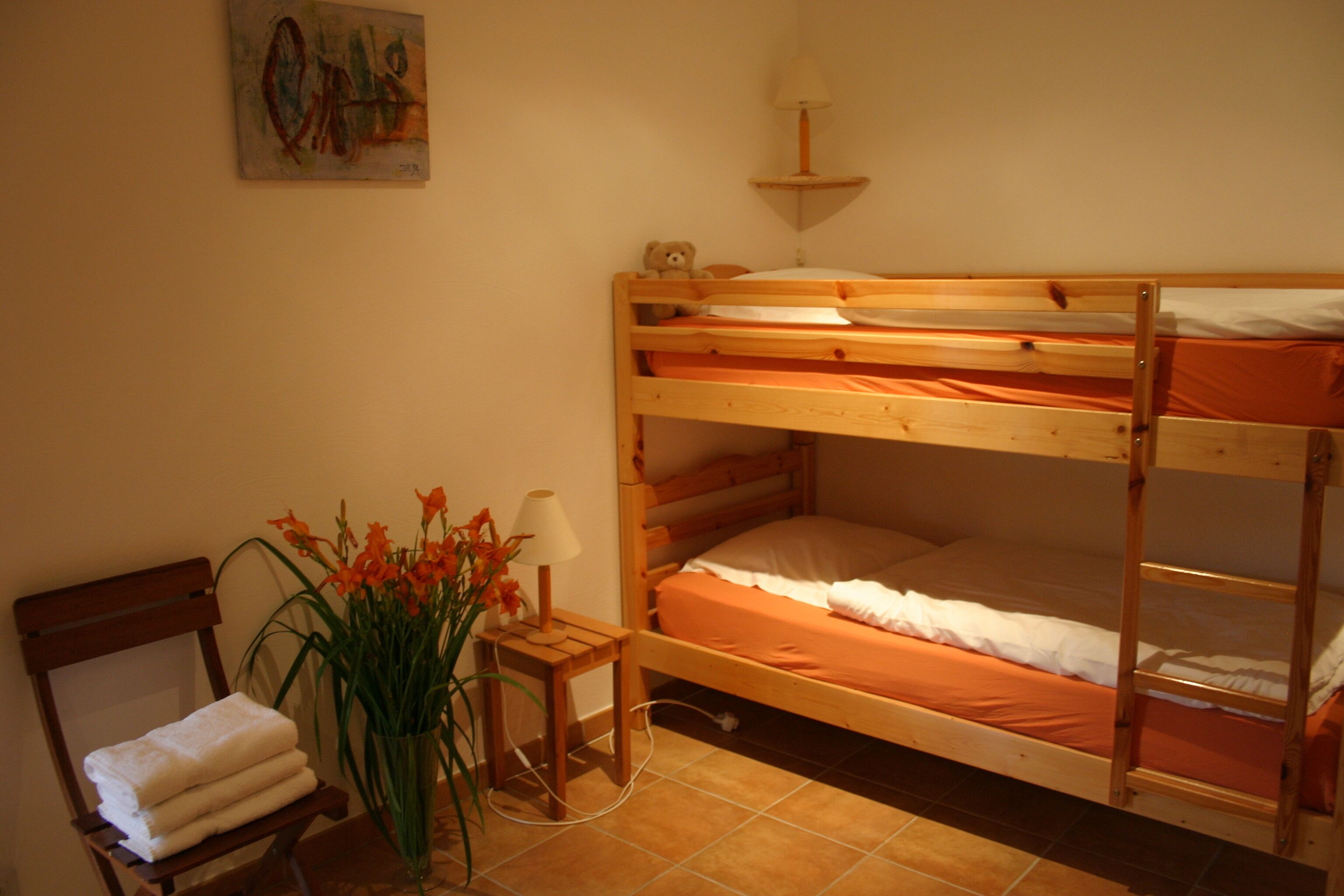 A bunk bed room with a chair and a small table with a lamp.