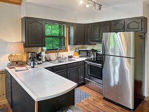 Une cuisine moderne avec des meubles de couleur sombre, des appareils en acier inoxydable et une fenêtre donnant sur un espace verdoyant.