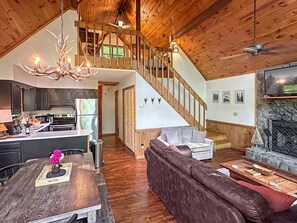 A spacious living area with a wooden staircase, a fireplace, and a kitchen with modern appliances.