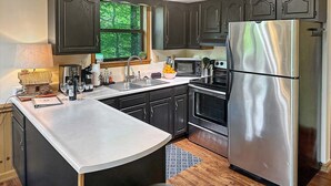 Una cocina moderna con armarios oscuros, electrodomésticos de acero inoxidable, una isla grande y un ventanal con vistas a árboles.