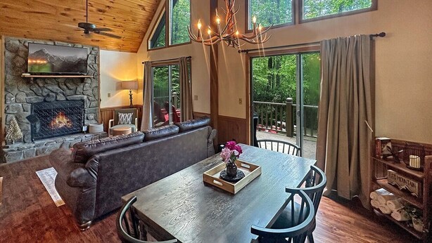 Una sala de estar acogedora con chimenea de piedra, un ventanal grande y un comedor con mesa y sillas.