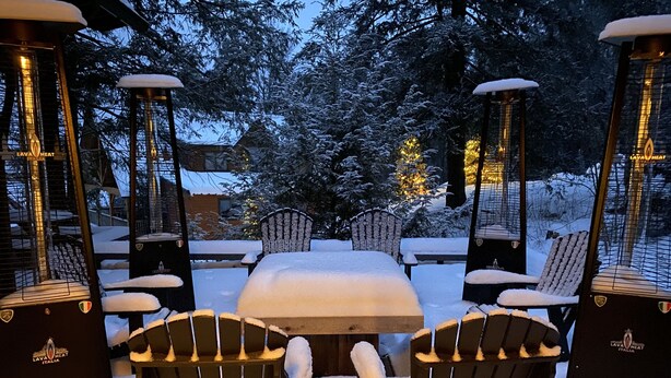 Ett utomhusområde med sittplatser, där ett snötäckt bord och stolar står omgivna av höga värmeelement.