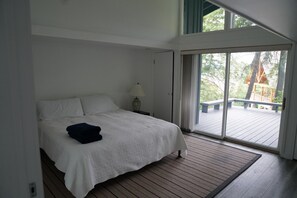 Ett sovrum med en stor säng, ett nattduksbord med en lampa och en skjutdörr i glas som leder ut till en uteplats.