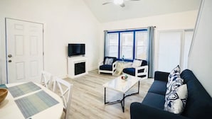 A living room with a TV, sofa, and a ceiling fan. - Santorini Cave Style Cottage with Fenced-in Yard (Chapel Hill)